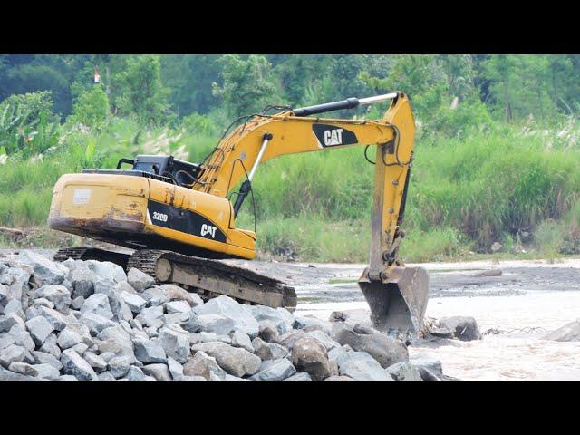 Caterpilar 320D Excavators and dump trucks continue to work hard to move large rocks to create a dam