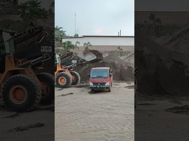 bulldozers load sand into small trucks 