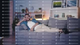 Carefree Middle Eastern guy watching TV laughing lying on couch in dark house