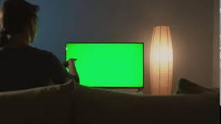 woman is sitting on the couch watching tv with a green screen switching channels with a