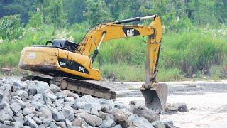 Caterpilar 320D Excavators and dump trucks continue to work hard to move large rocks to create a dam