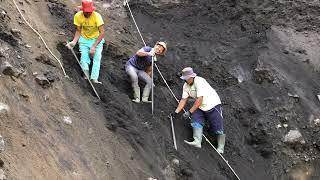 Teamwork of three miners to drop a boulder from a cliff