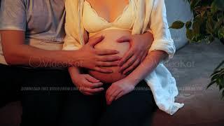 Pregnant woman and a man touch tenderly belly and hugging sitting on a sofa in close-up